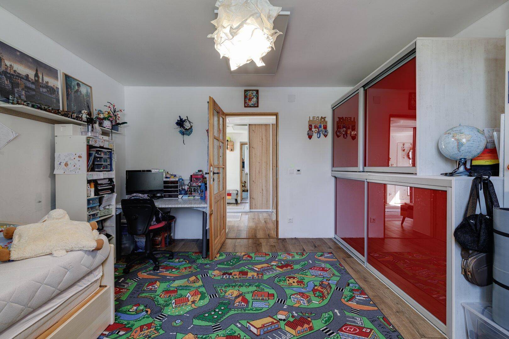 Funktionales Kinderzimmer mit Schreibtisch, Stauraum und einem modernen roten Spiegelschrank.
