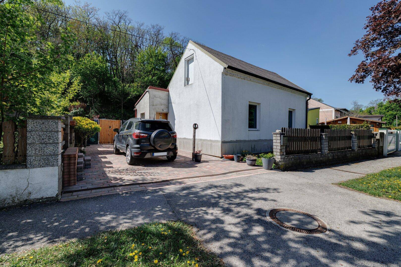 Ansicht des Hauses von der Straße mit Einfahrt, gepflastertem Parkplatz und Zaun.