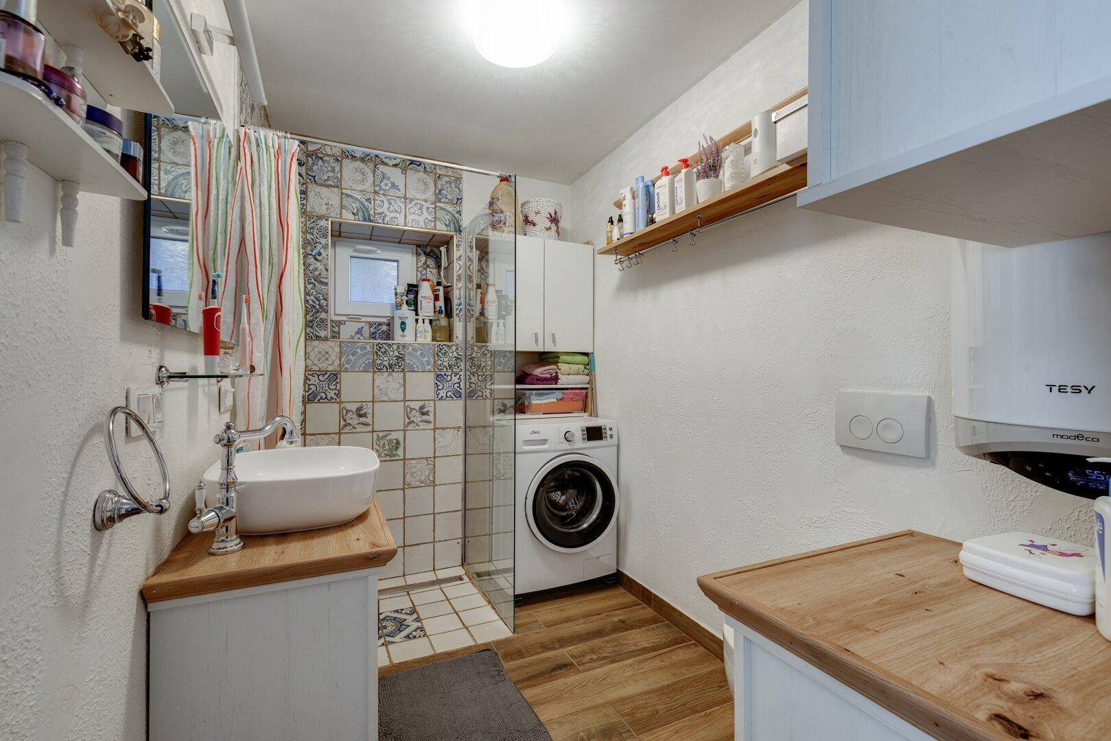 Modernes Badezimmer mit Dusche, Waschbecken auf Holzunterschrank und Waschmaschine.