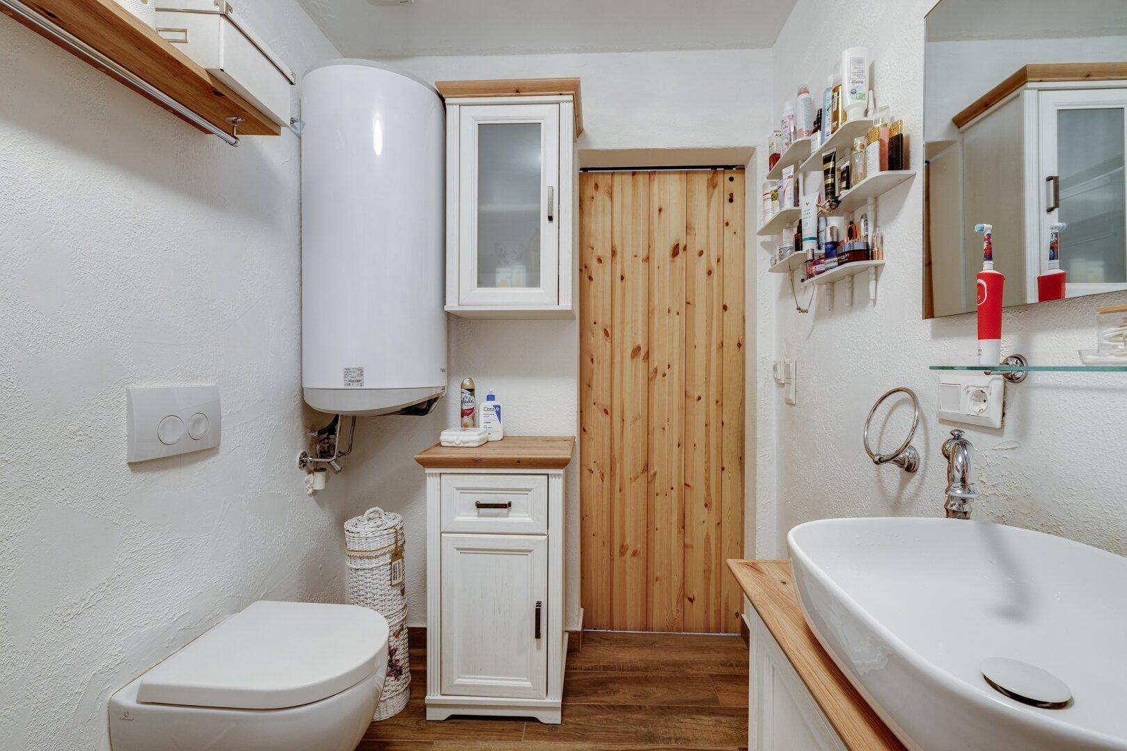 Badezimmer mit WC, modernem Waschbecken auf Holzunterschrank und Warmwasserboiler.
