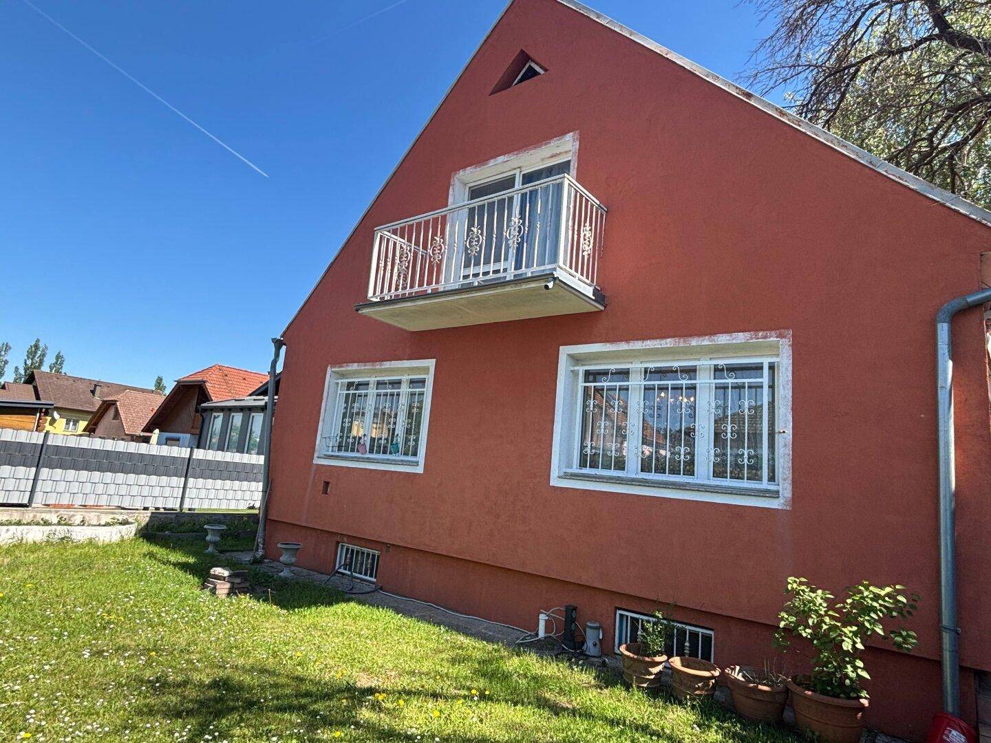 Rotes Haus mit kleinem Balkon und weißem Geländer unter strahlend blauem Himmel.