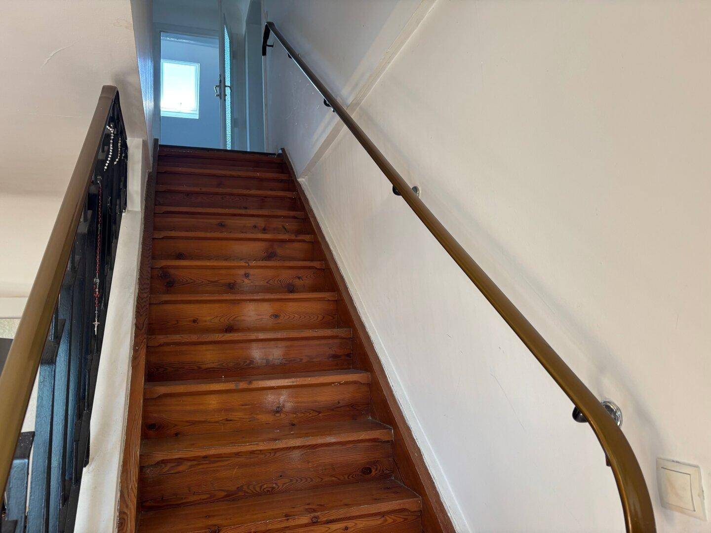 Holztreppe mit Handlauf führt in den oberen Bereich des Hauses.