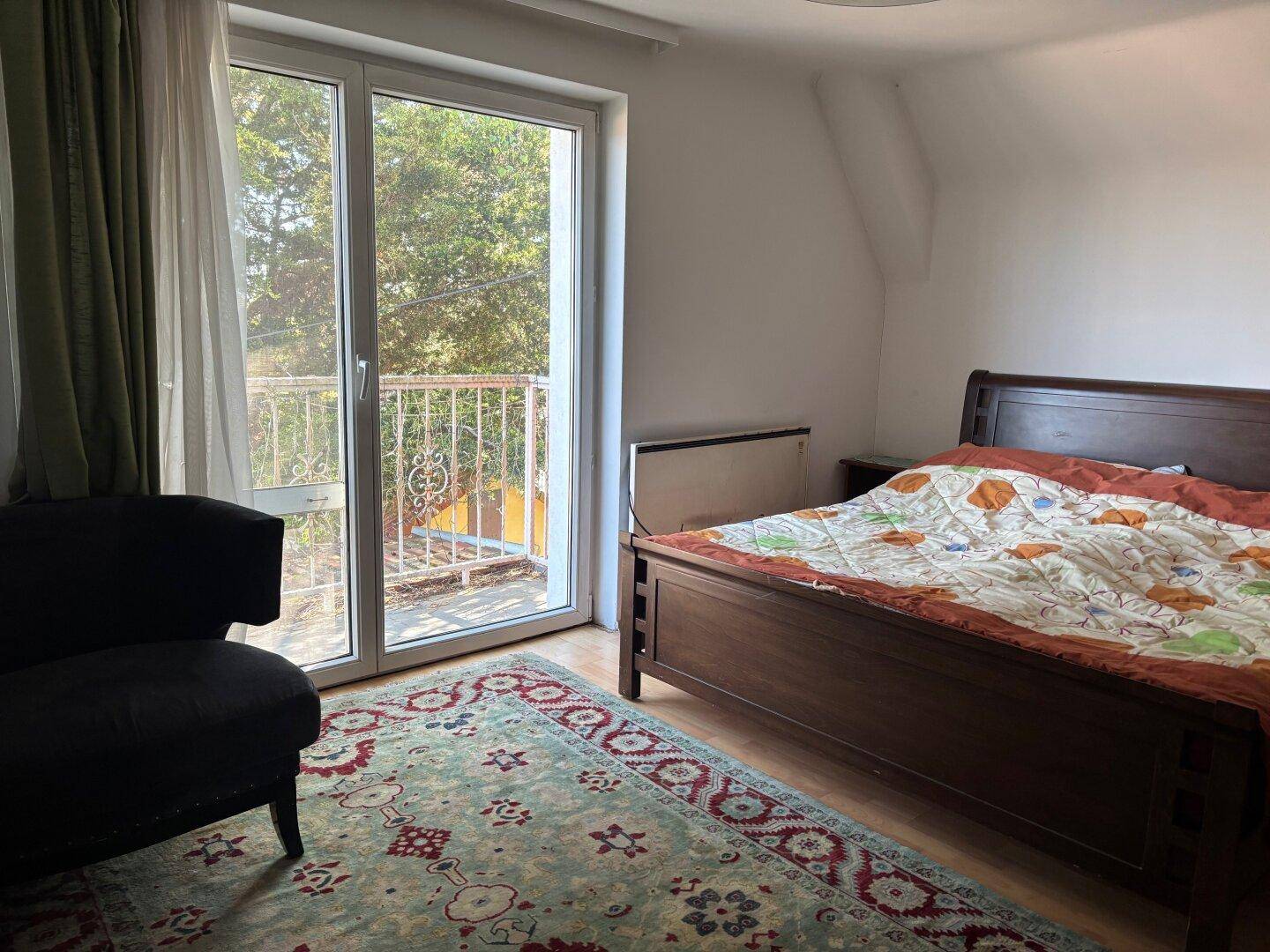 Schlafzimmer mit Holzbett, Teppich und Zugang zu einem kleinen Balkon.