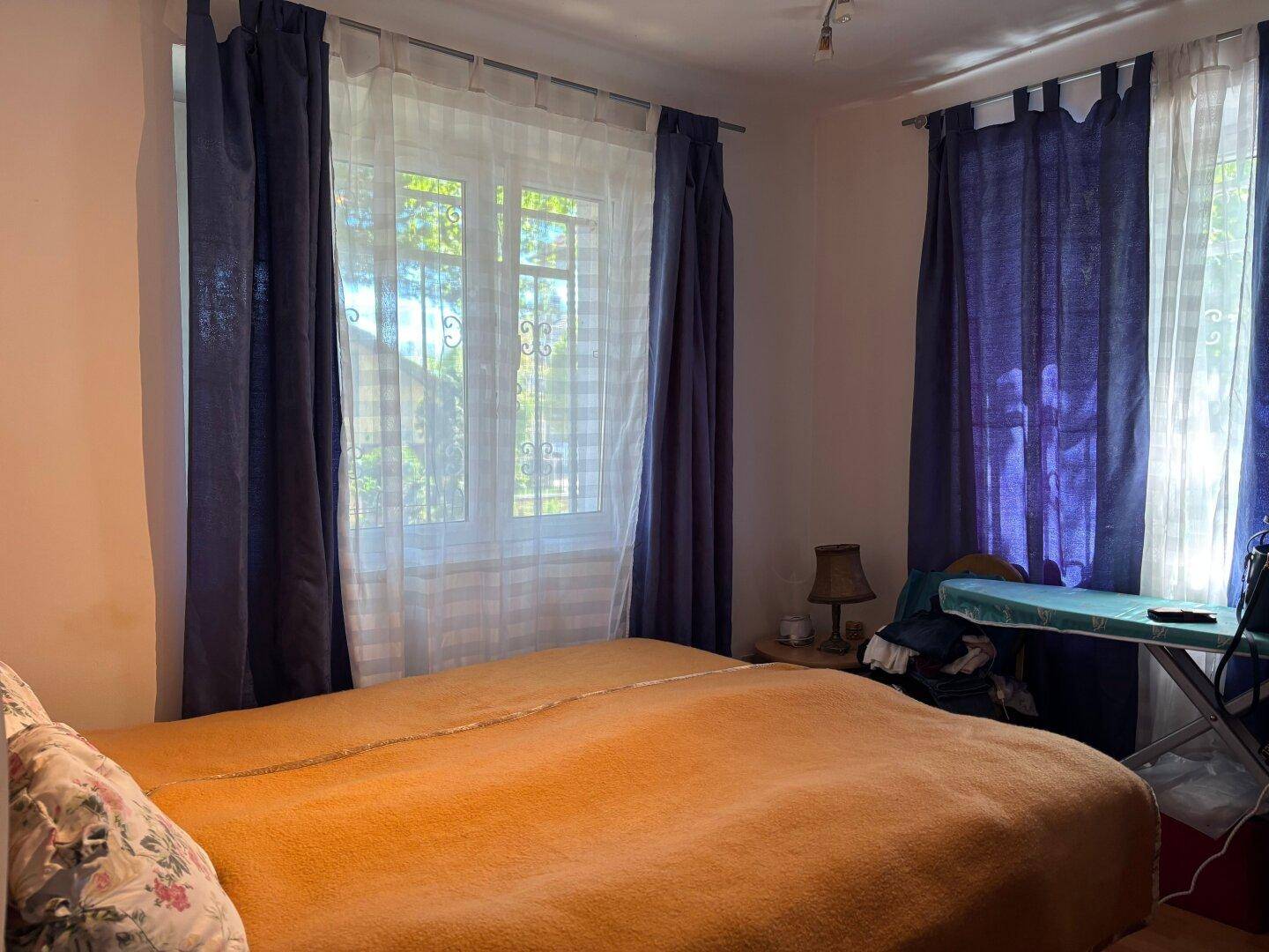 Schlafzimmer mit großem Bett, Holzboden und Fenster mit blauen Vorhängen.