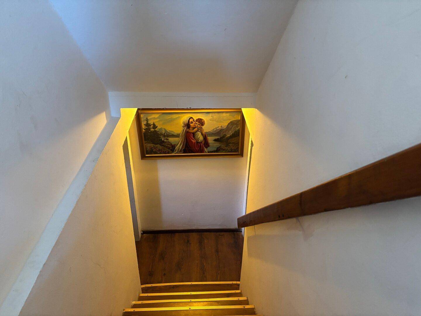 Treppenabgang mit Holzstufen und indirekter Beleuchtung an der Wand.