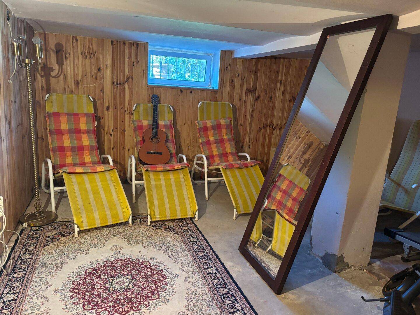 Ausgebauter Kellerraum mit Holzverkleidung, Liegestühlen und Teppich.