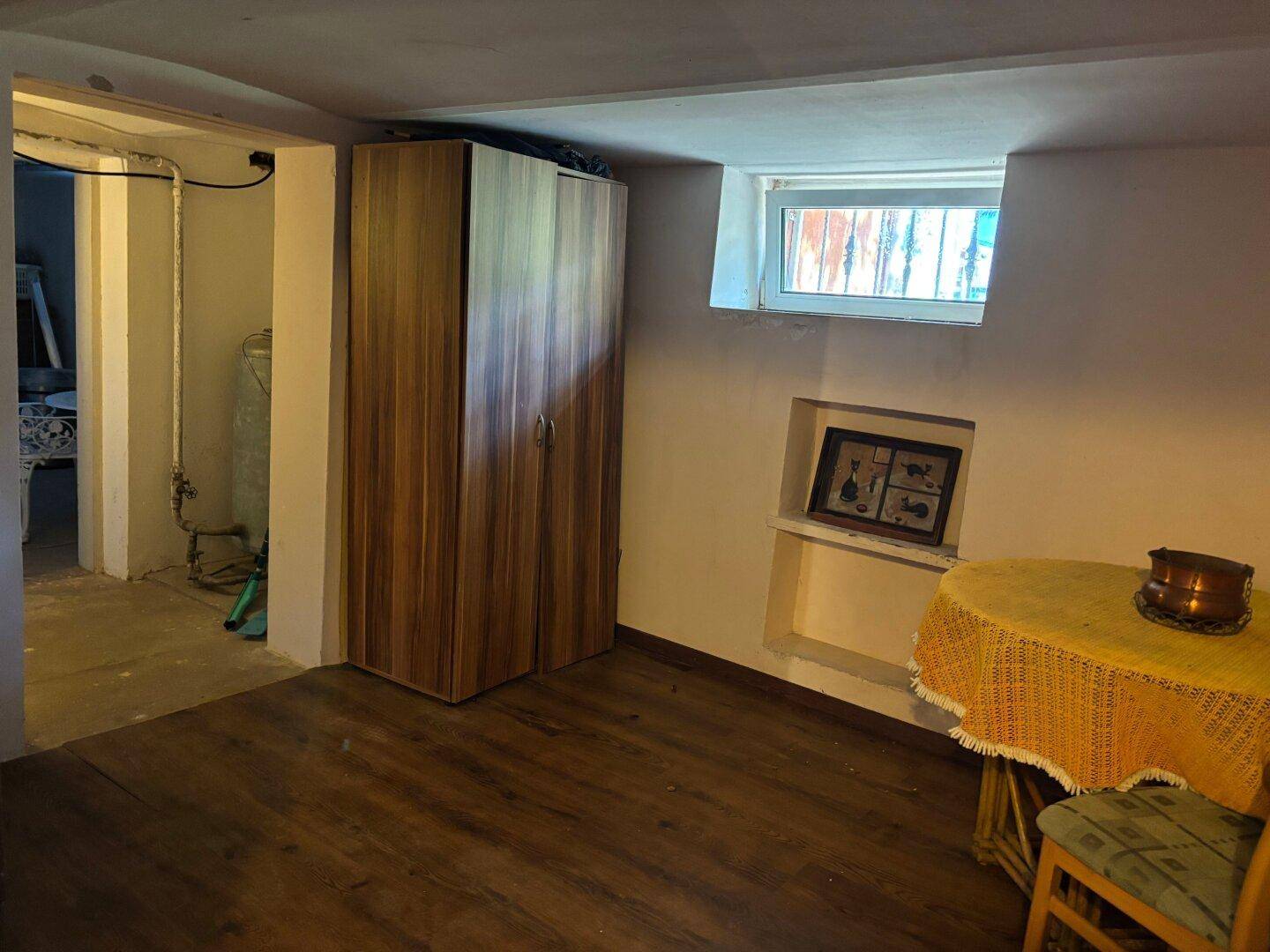 Kellerraum mit Holzboden, Schrank und kleinem Fenster, als Abstellraum genutzt.