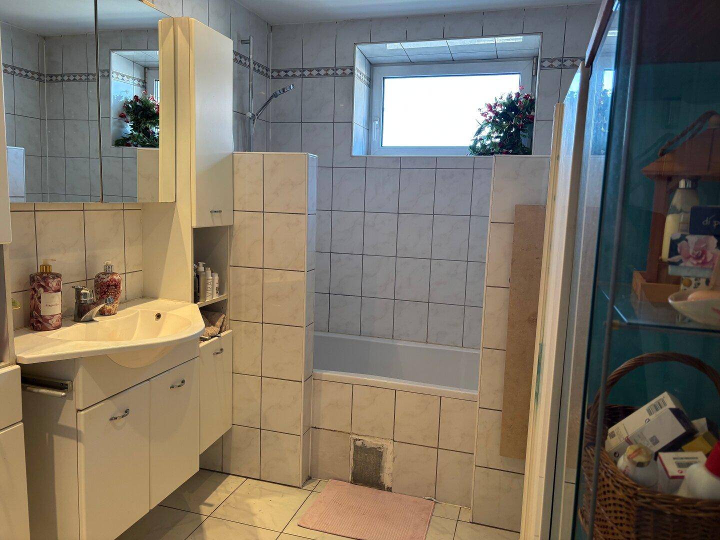 Badezimmer mit Badewanne, Waschbecken und Fenster, gefliest in hellen Tönen.