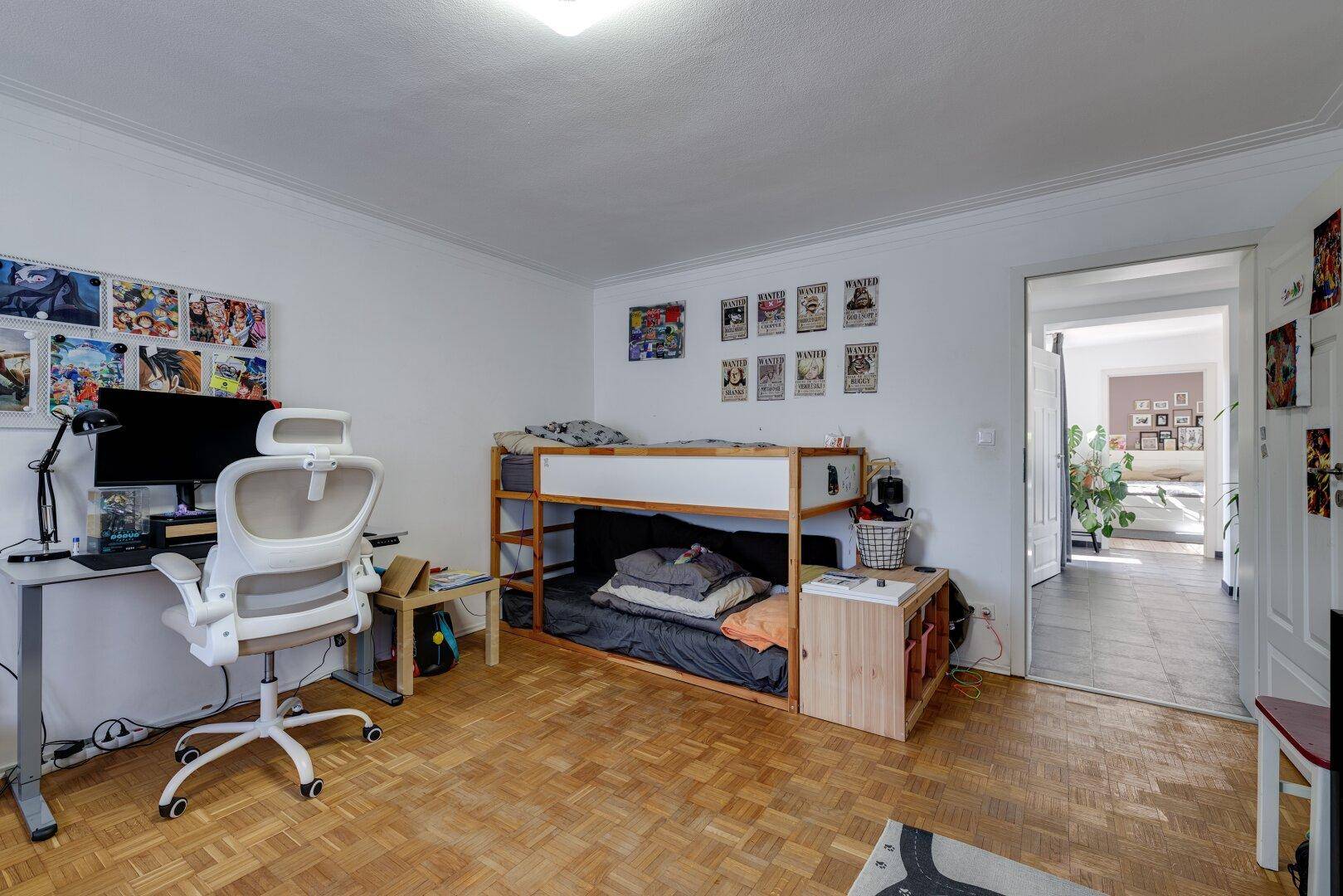 Helles Kinderzimmer mit Schreibtisch, Hochbett und Zugang zum Flur.