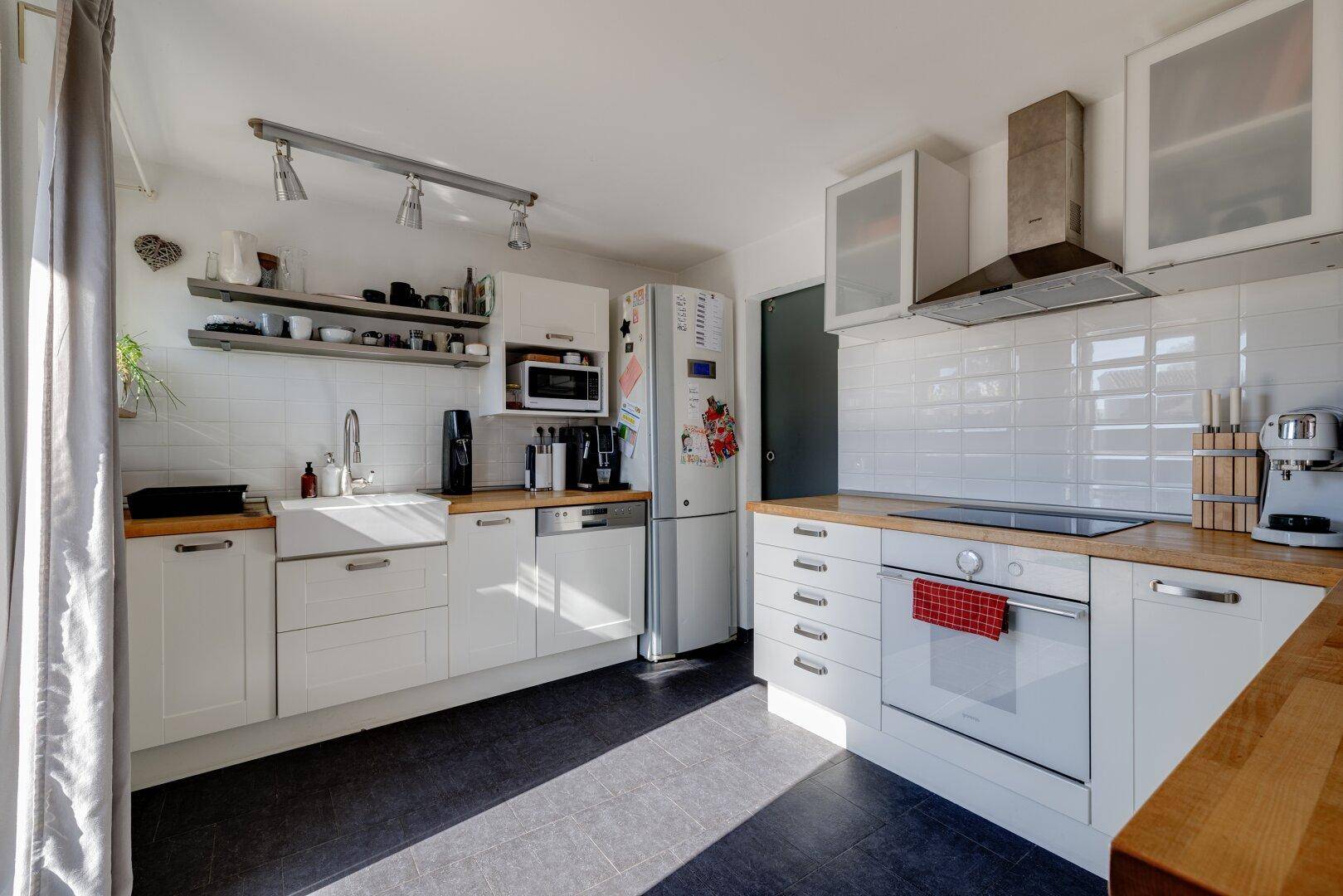 Funktionale Küche mit weißen Schränken, Holz-Arbeitsplatten und modernen Geräten.