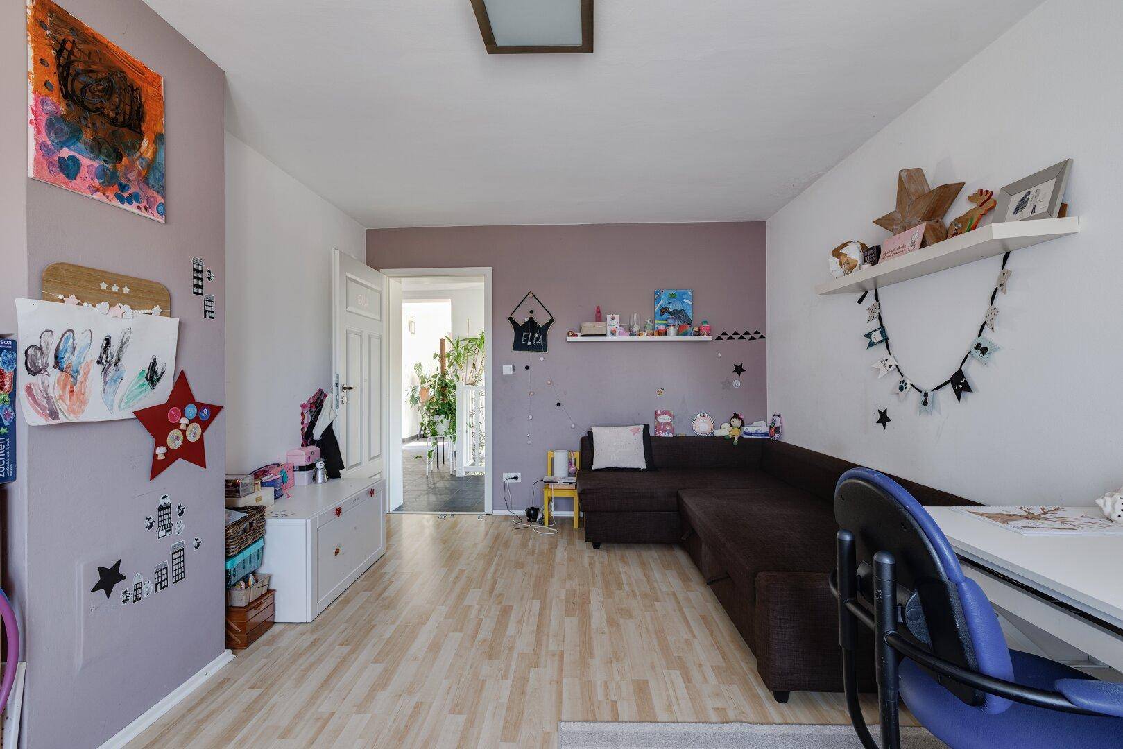 Helles Kinderzimmer mit Schlafsofa, Spielbereich und farbenfroher Dekoration.