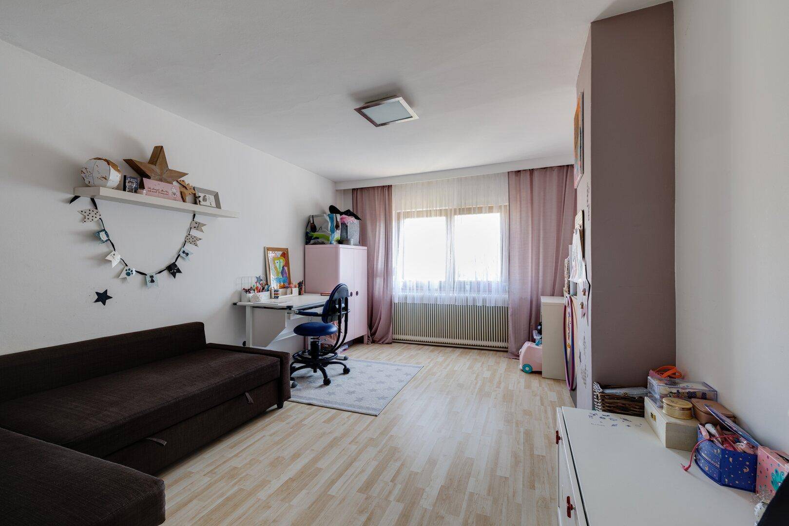 Freundliches Kinderzimmer mit Schlafsofa, Schreibtisch und hellem Holzboden.