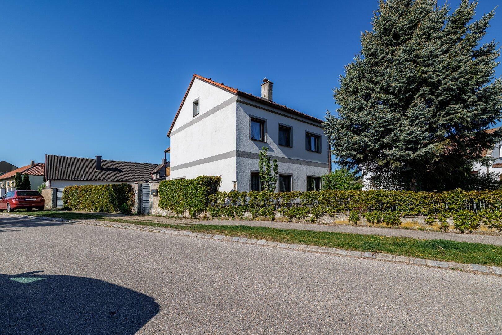 Einfamilienhaus mit weißer Fassade, Satteldach und gepflegtem Vorgarten an einer ruhigen Straße.