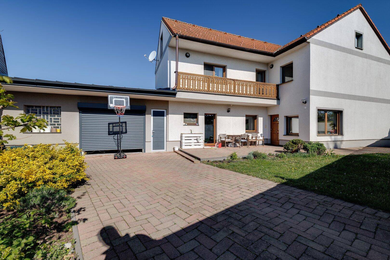 Ansicht des Hauses von außen mit Balkon, Garage und gepflasterter Zufahrt.