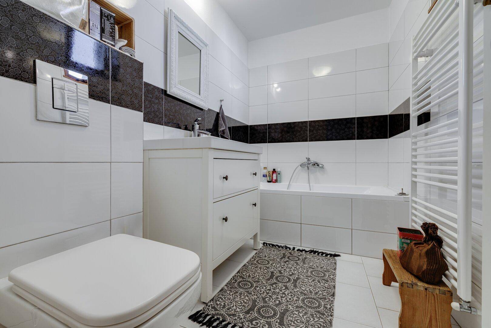 Helles Badezimmer mit WC, Badewanne und modernen Fliesen in Schwarz-Weiß.
