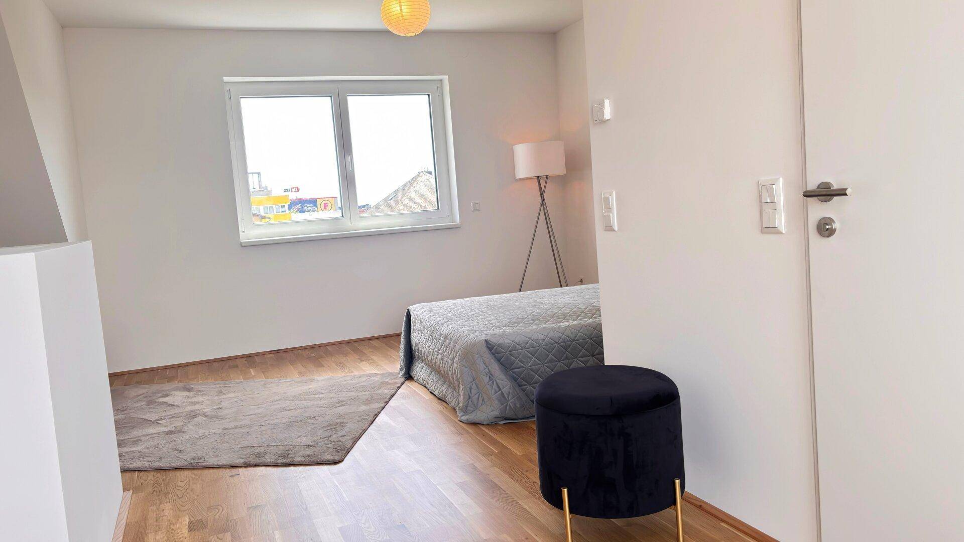 Schlafzimmer im Dachgeschoss mit schräger Decke, Holzboden und einem Fenster.