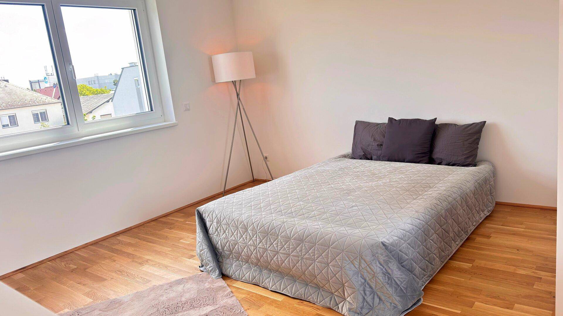 Helles Schlafzimmer mit Holzboden, Doppelbett und einer modernen Stehlampe.