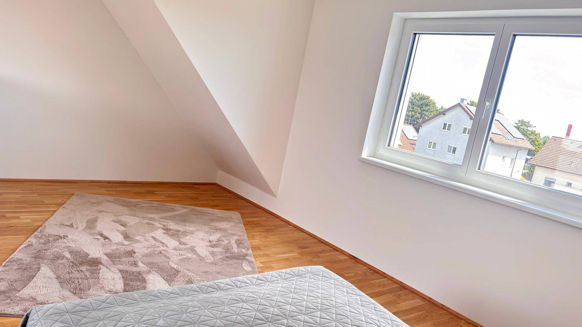 Schlafzimmer im Dachgeschoss mit schräger Decke, Holzboden und einem Fenster mit Ausblick.