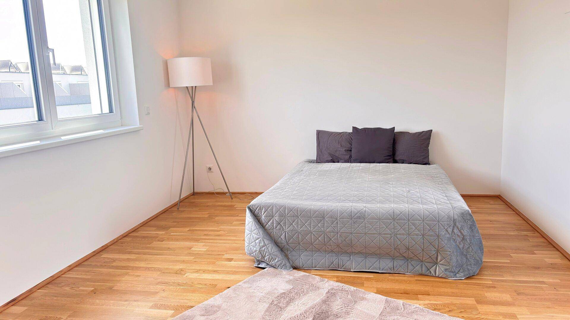 Schlafzimmer mit Holzboden, Doppelbett und einer modernen Stehlampe, gut beleuchtet.