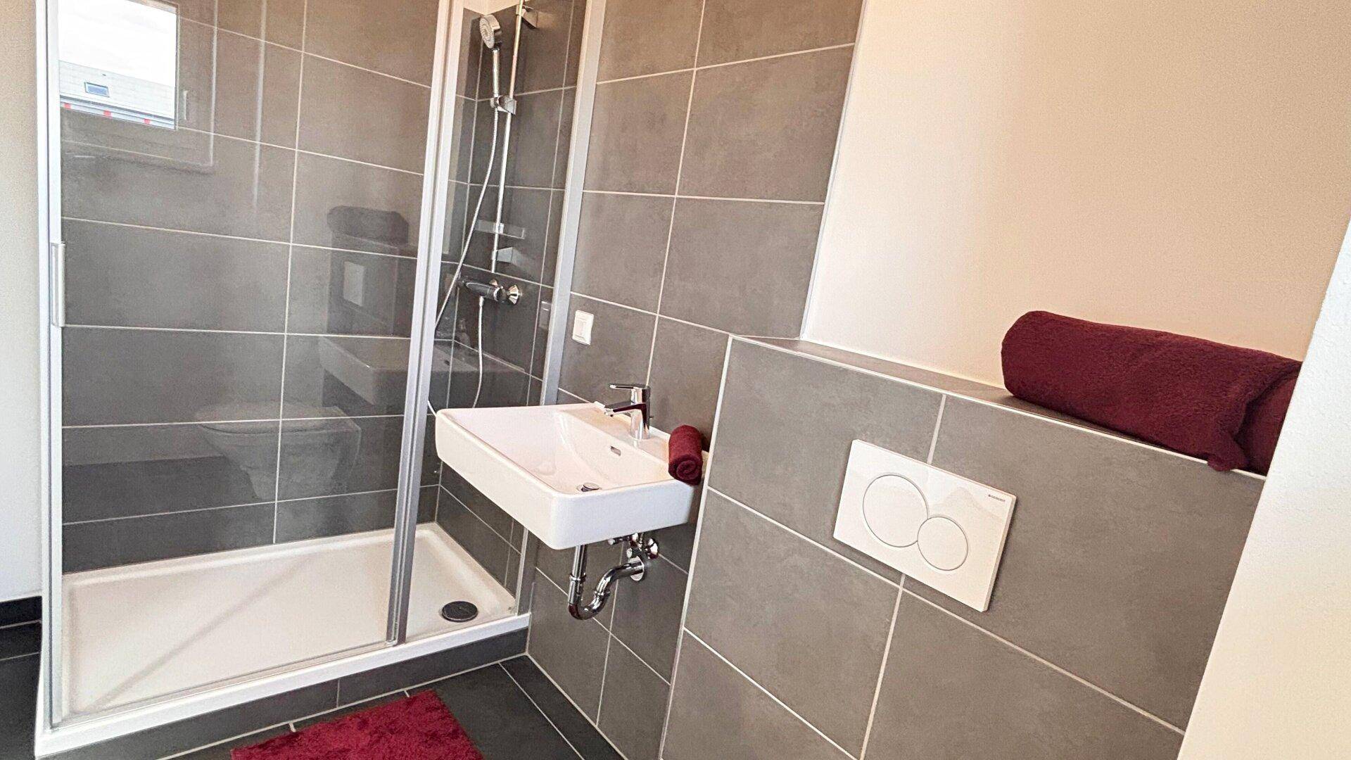 Funktionales Badezimmer mit Duschkabine, Waschbecken und Fenster für Tageslicht.