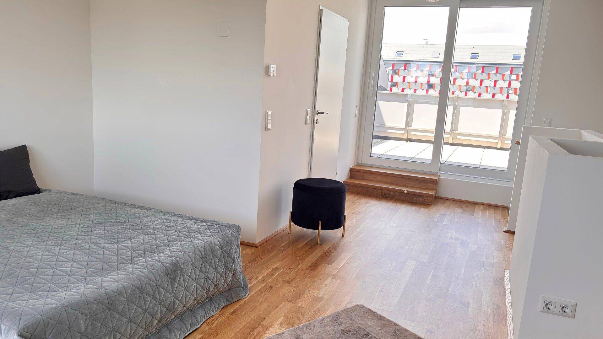 Helles Schlafzimmer mit Holzboden und Zugang zu einer großen Terrasse im Freien.