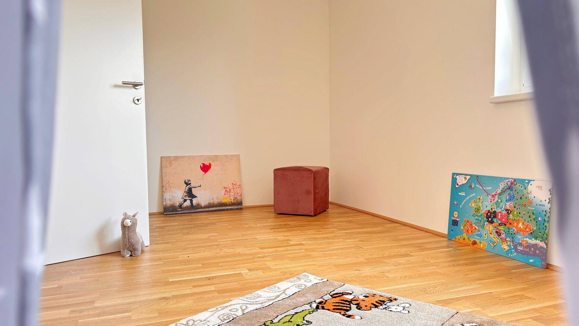 Kinderzimmer mit Holzboden und moderner Dekoration, gesehen durch eine offene Tür.