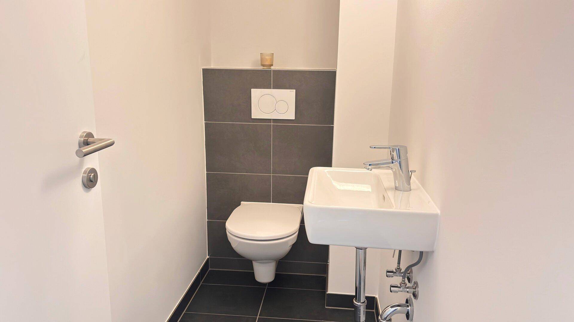 Modernes Gäste-WC mit Wand-WC, kleinem Waschbecken und dunklen Bodenfliesen.