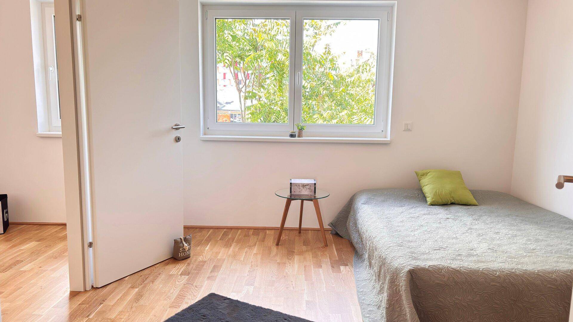 Schlafzimmer mit Einzelbett, Holzboden und großem Fenster mit Blick ins Grüne.