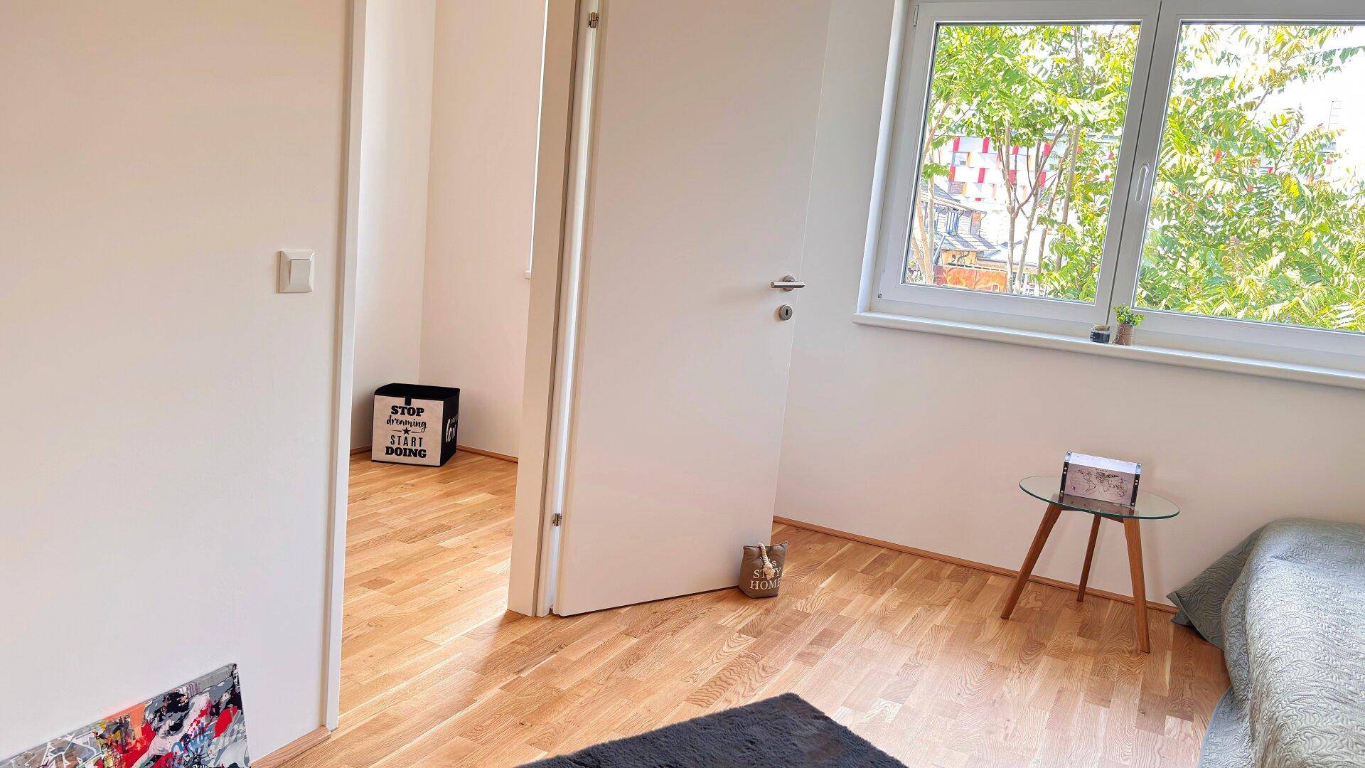 Schlafzimmer mit Holzboden und offener Tür zu einem angrenzenden Raum, hell und freundlich.