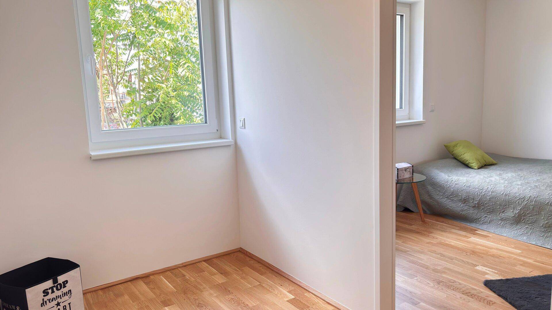 Schlafzimmer mit Holzboden und einem Fenster, das viel Tageslicht hereinlässt.