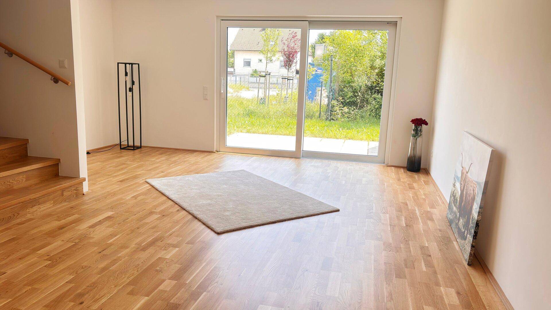 Helles Wohnzimmer mit Parkettboden, Treppe und Zugang zu einer großen Glasschiebetür.