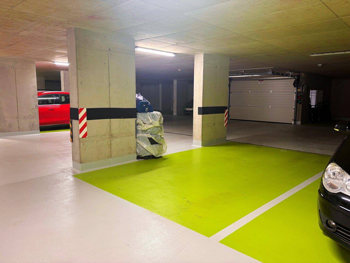 Tiefgarage mit markierten Stellplätzen und Zufahrtstor für Fahrzeuge.