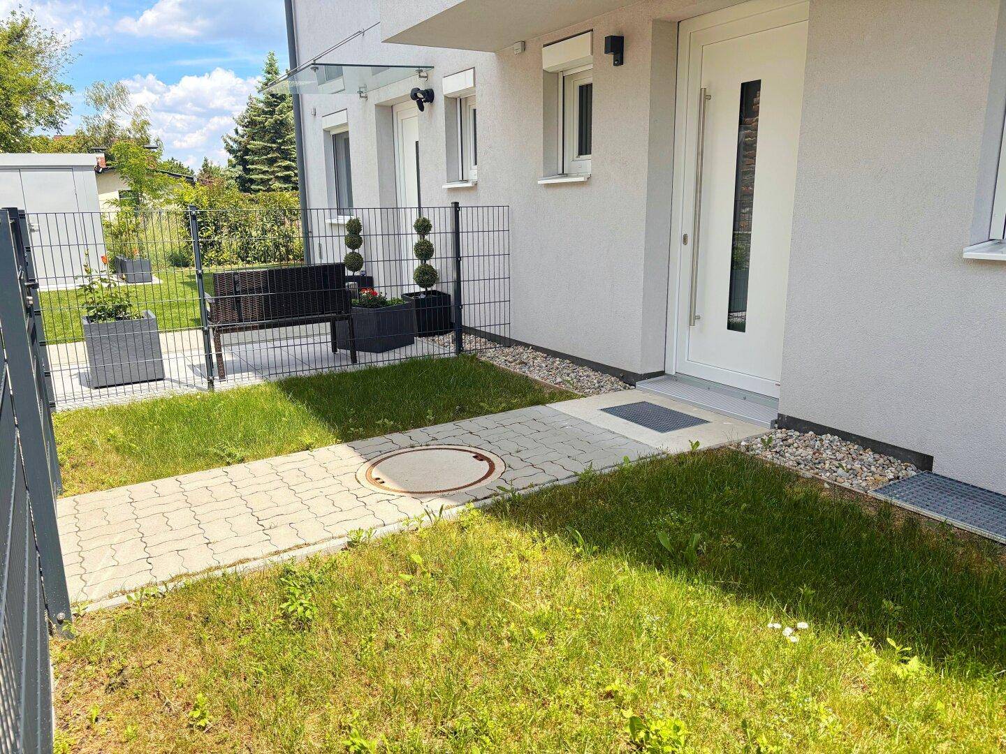 Eingangsbereich eines modernen Hauses mit gepflastertem Weg, Rasenfläche und dekorativen Pflanzen.