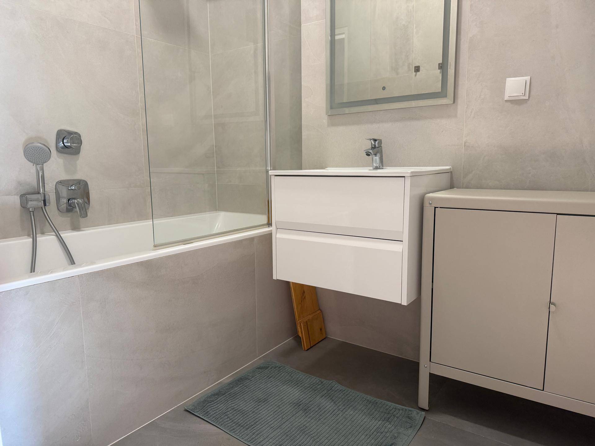 Helles Badezimmer mit Badewanne, integrierter Dusche und modernem Waschtisch mit Unterschrank.