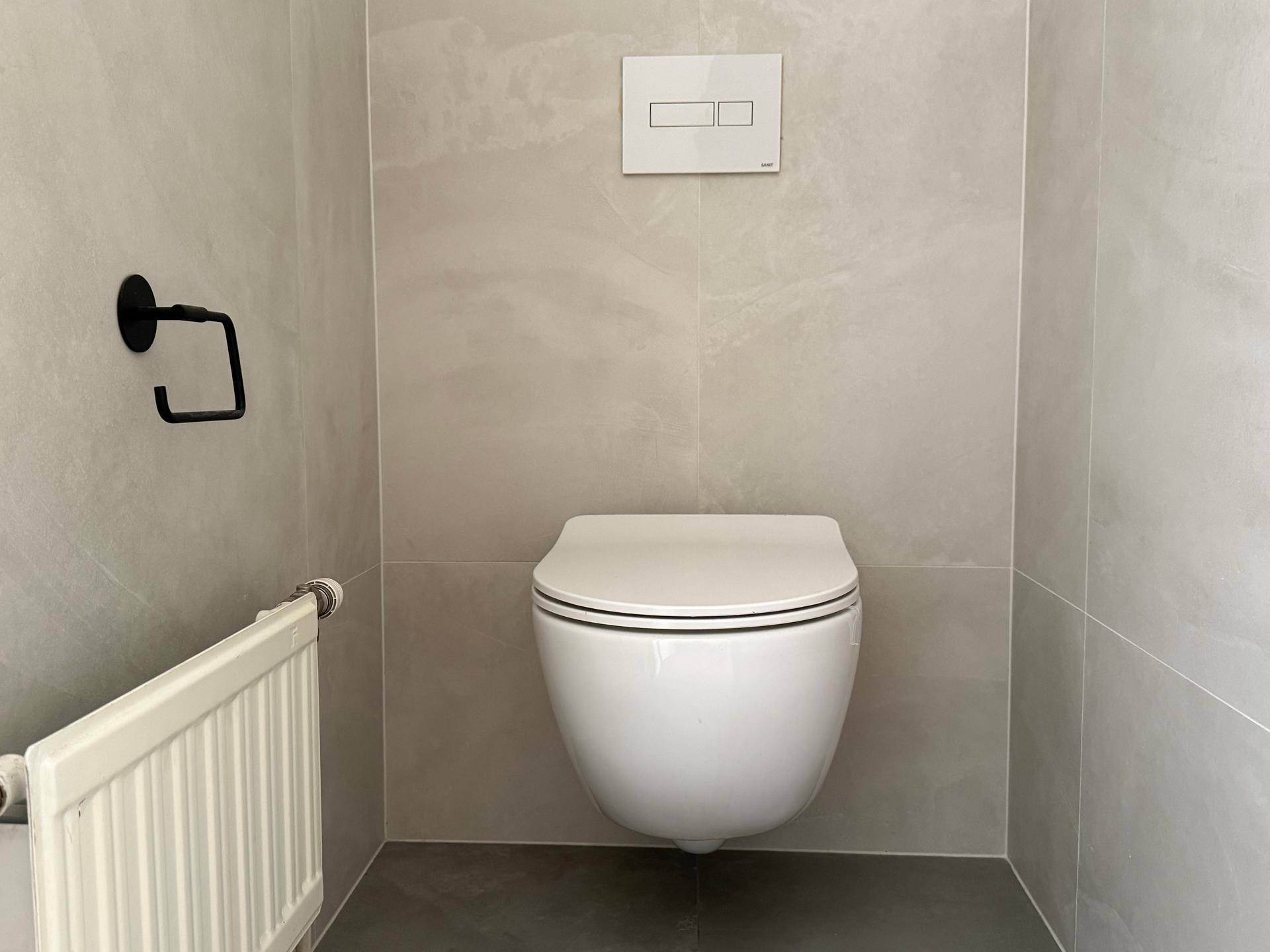 Modernes WC mit wandhängender Toilette und hellgrauen Fliesen an Wänden und Boden.