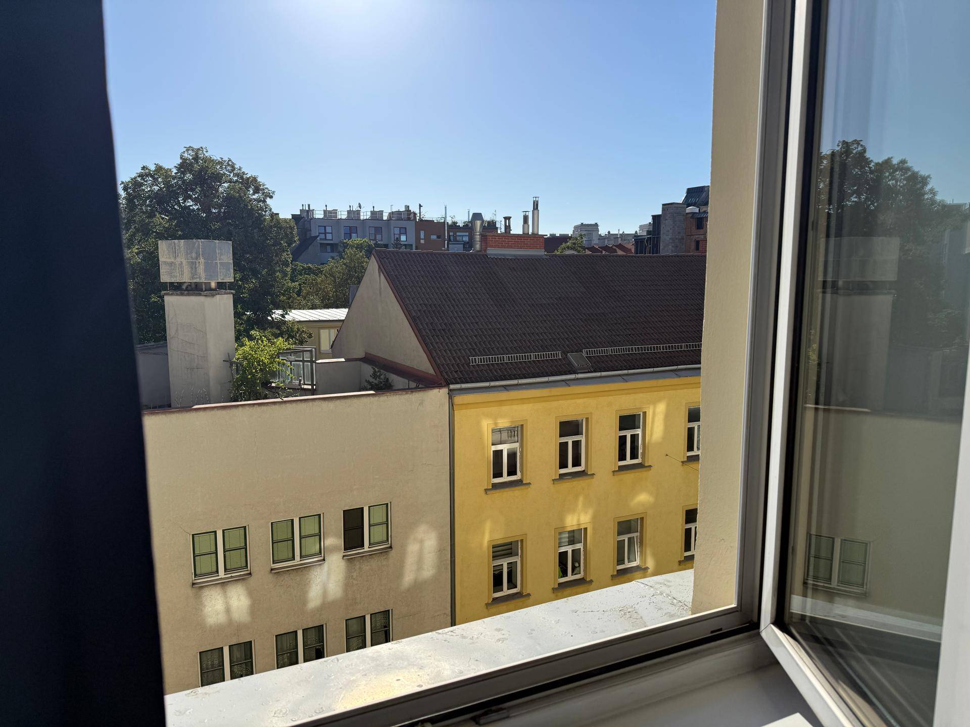Blick aus dem Fenster auf die umliegenden Gebäude und Dächer der Stadt an einem sonnigen Tag.