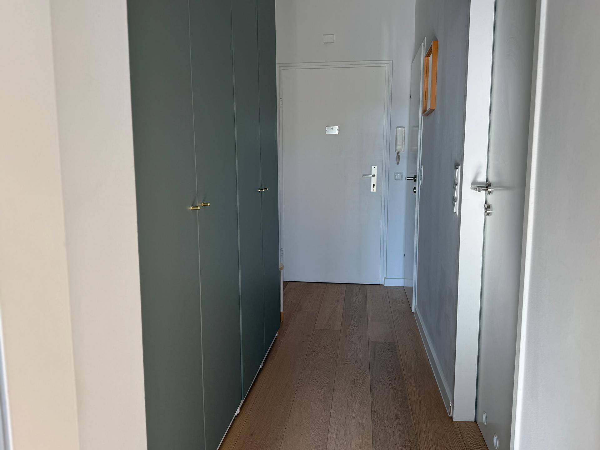 Heller Flur mit integrierten Schränken und Holzboden, der zum Eingangsbereich führt.