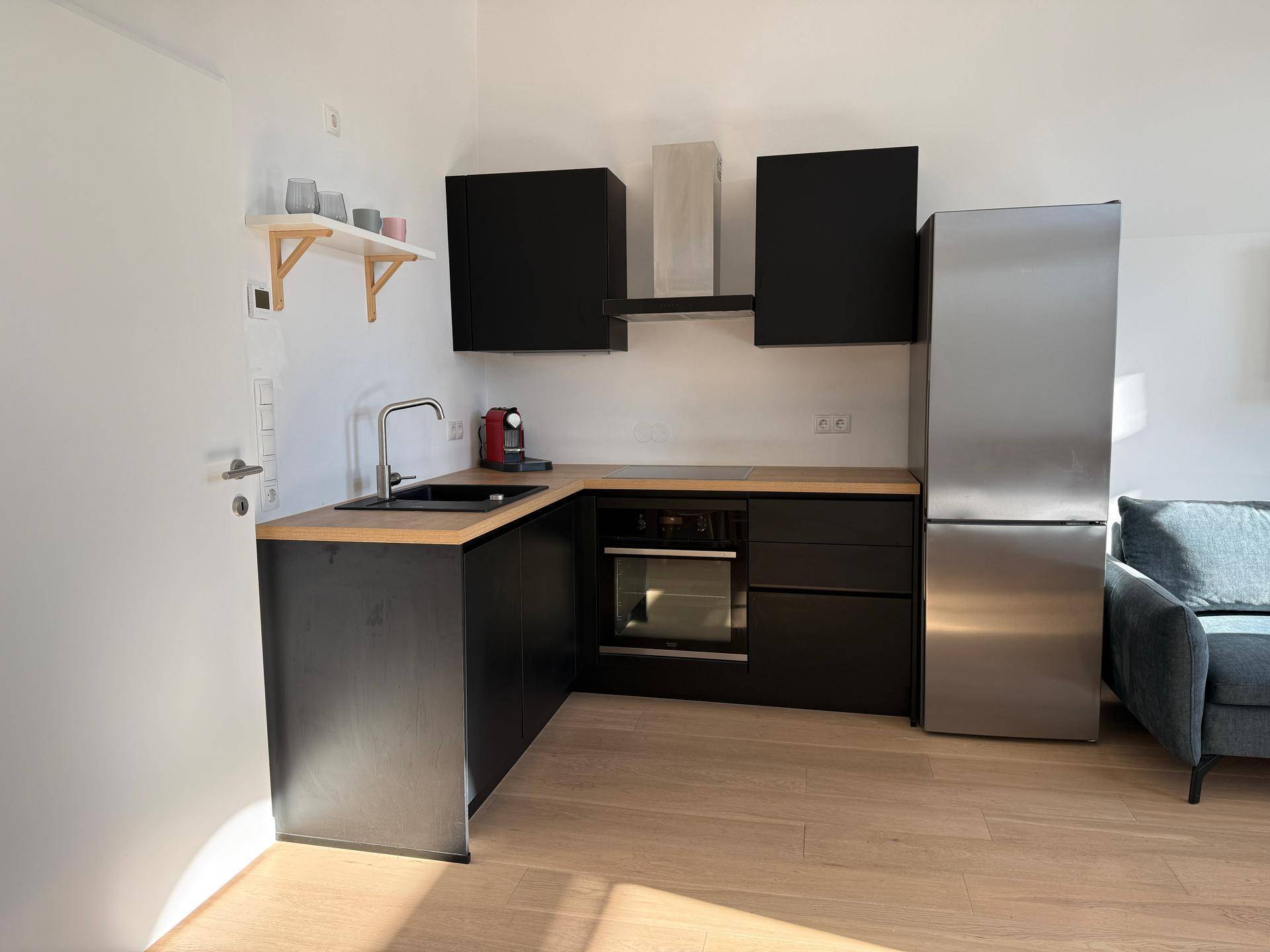 Kompakte Küchenzeile mit schwarzer Spüle, Holz-Arbeitsplatte und modernen Geräten in einem hellen Raum.