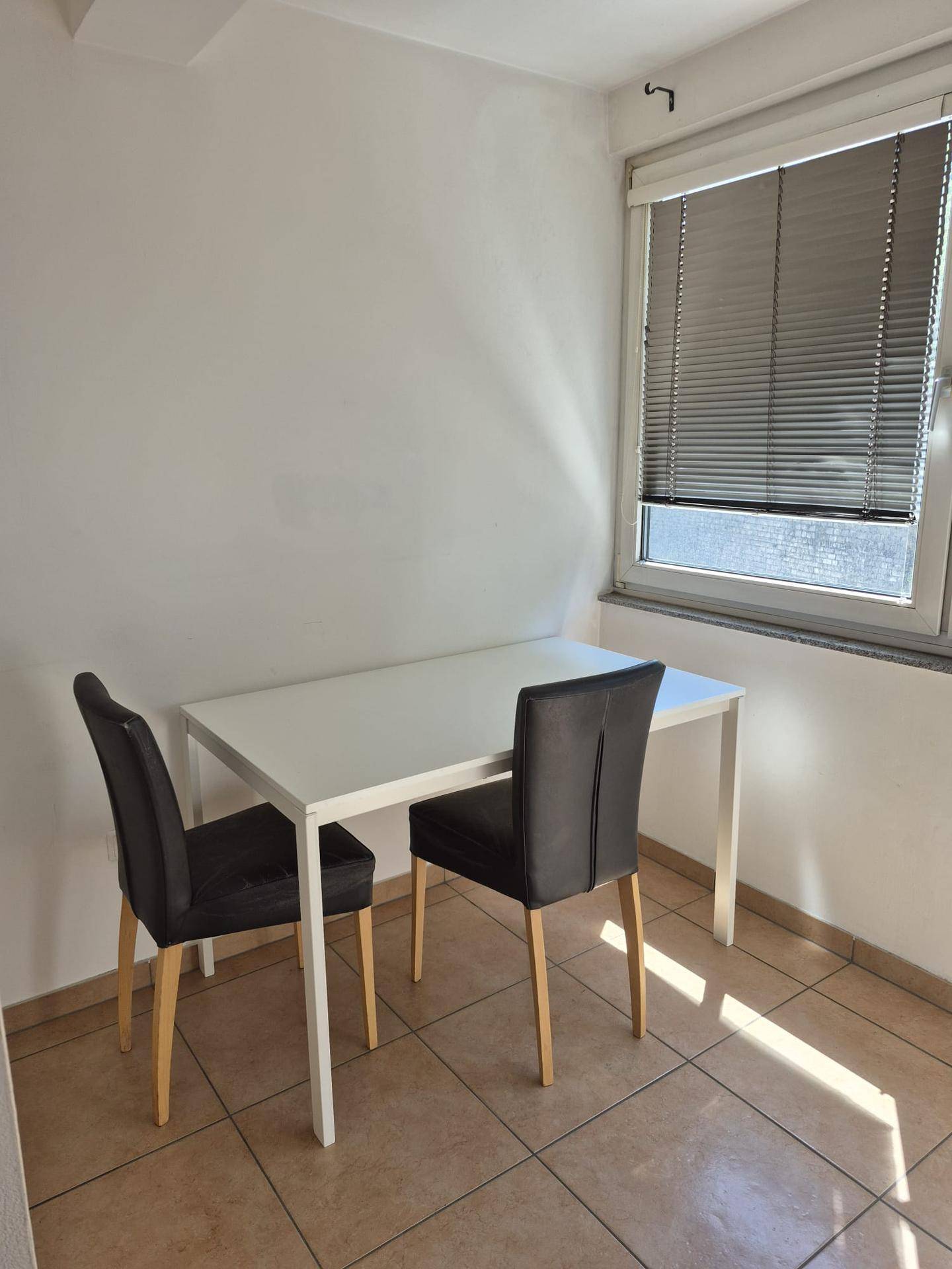Heller Essbereich mit weißem Tisch und zwei Stühlen neben einem Fenster.