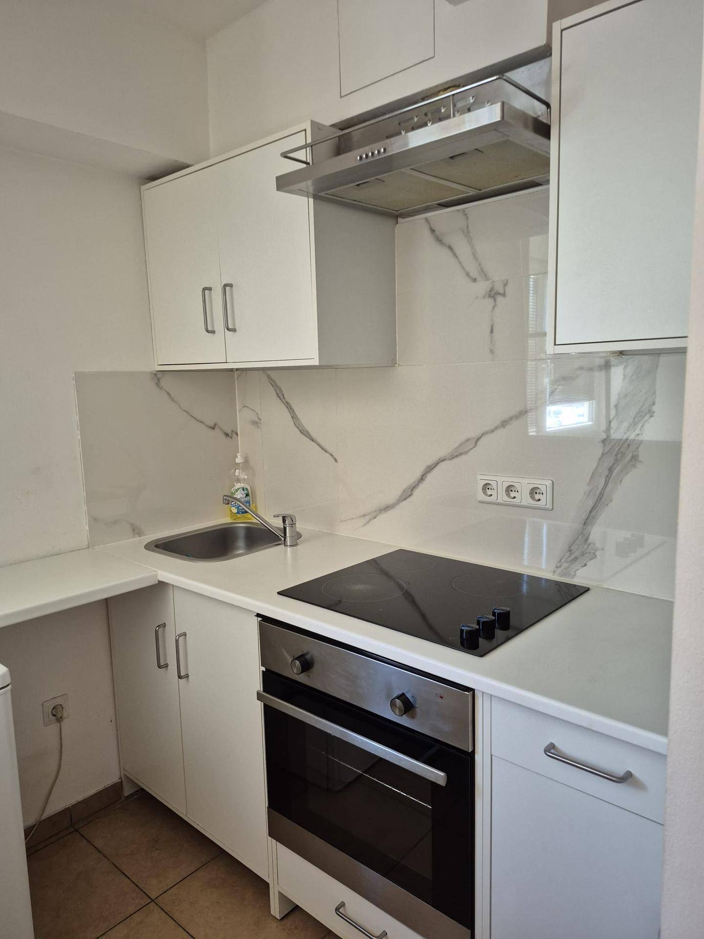 Moderne Küche mit weißen Schränken, Induktionskochfeld und Backofen.