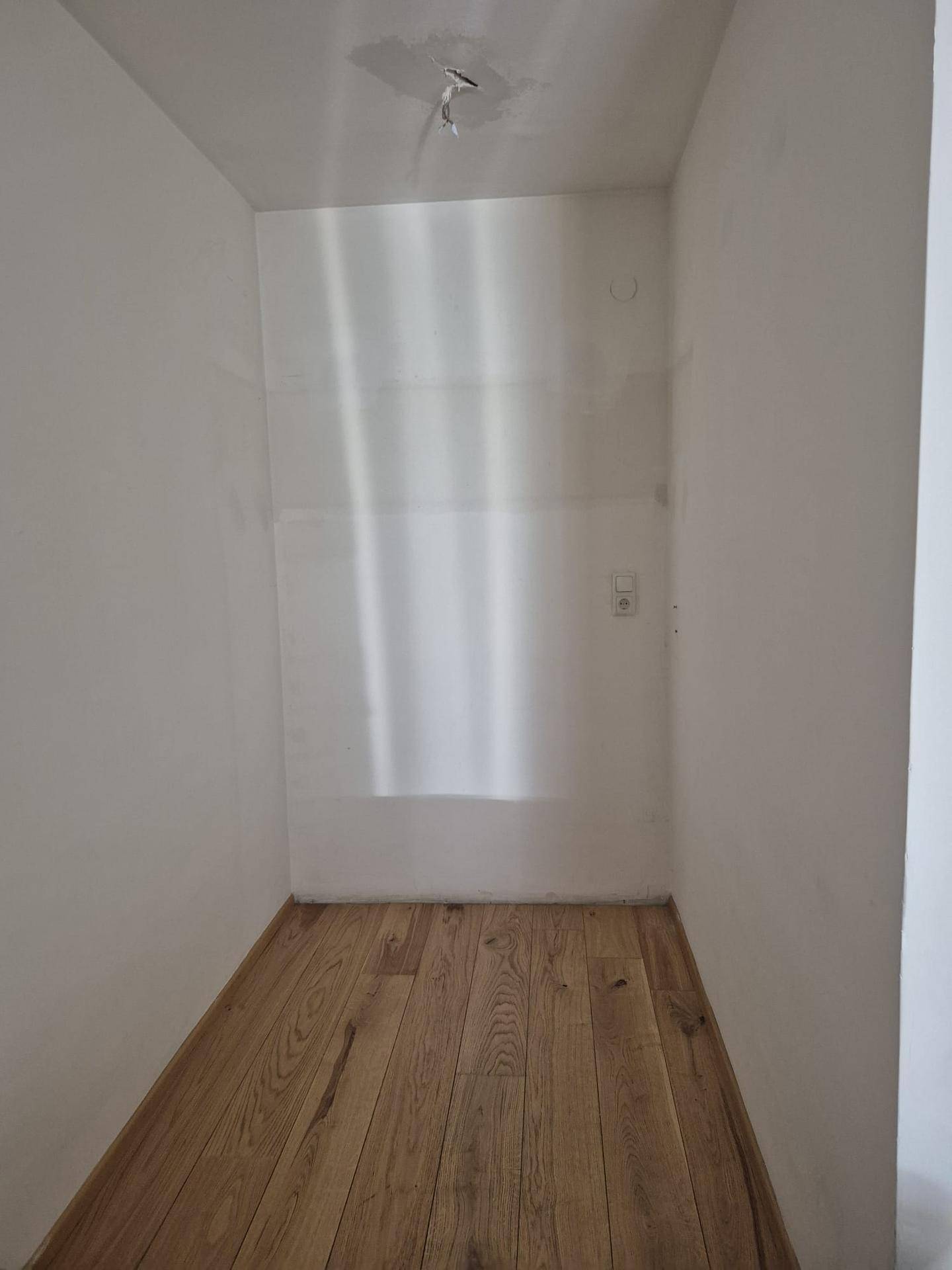 Kleiner, leerer Abstellraum mit hellem Holzfußboden und weißen Wänden.