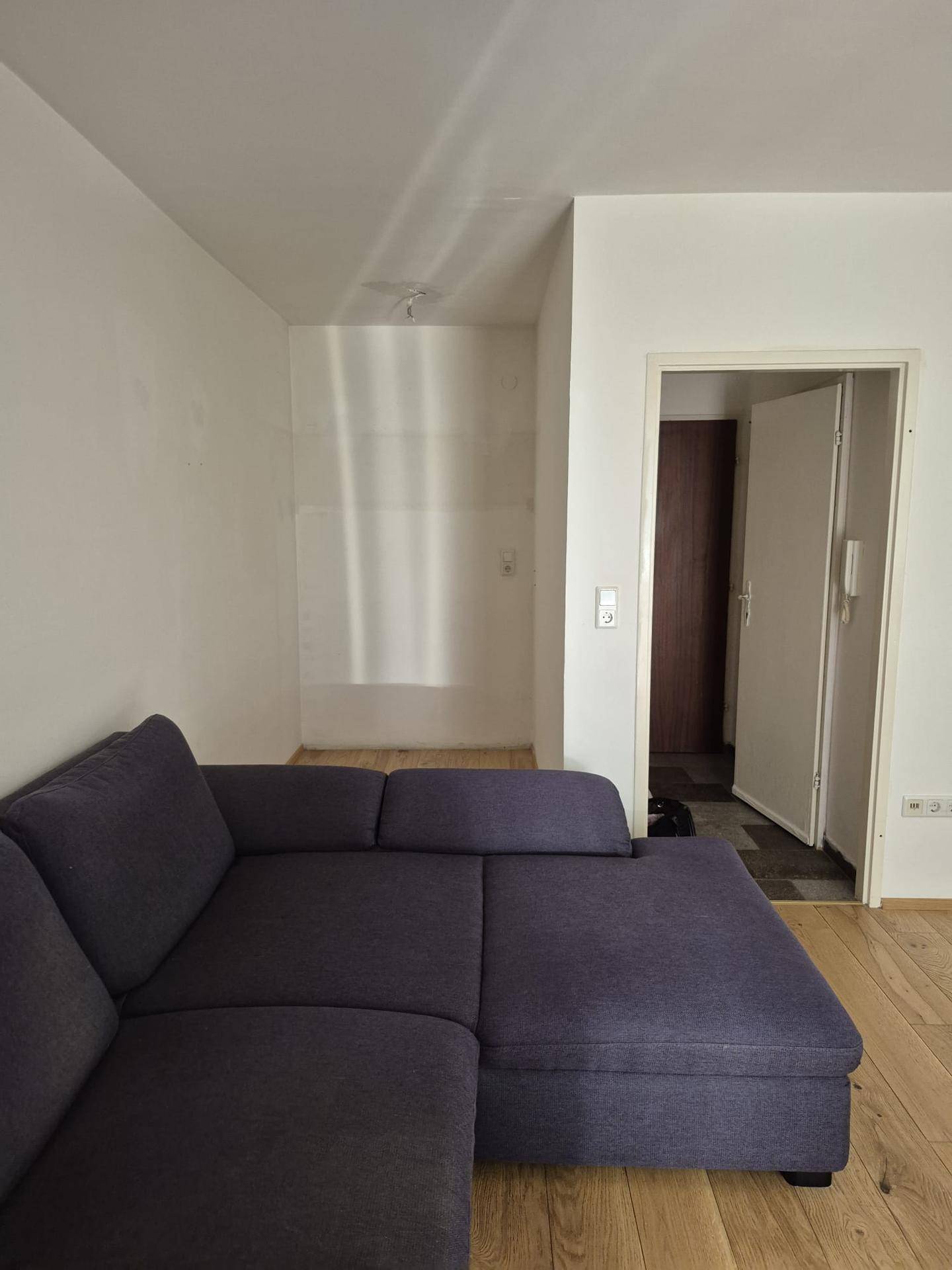 Gemütliches Wohnzimmer mit dunklem Ecksofa und hellem Holzfußboden.