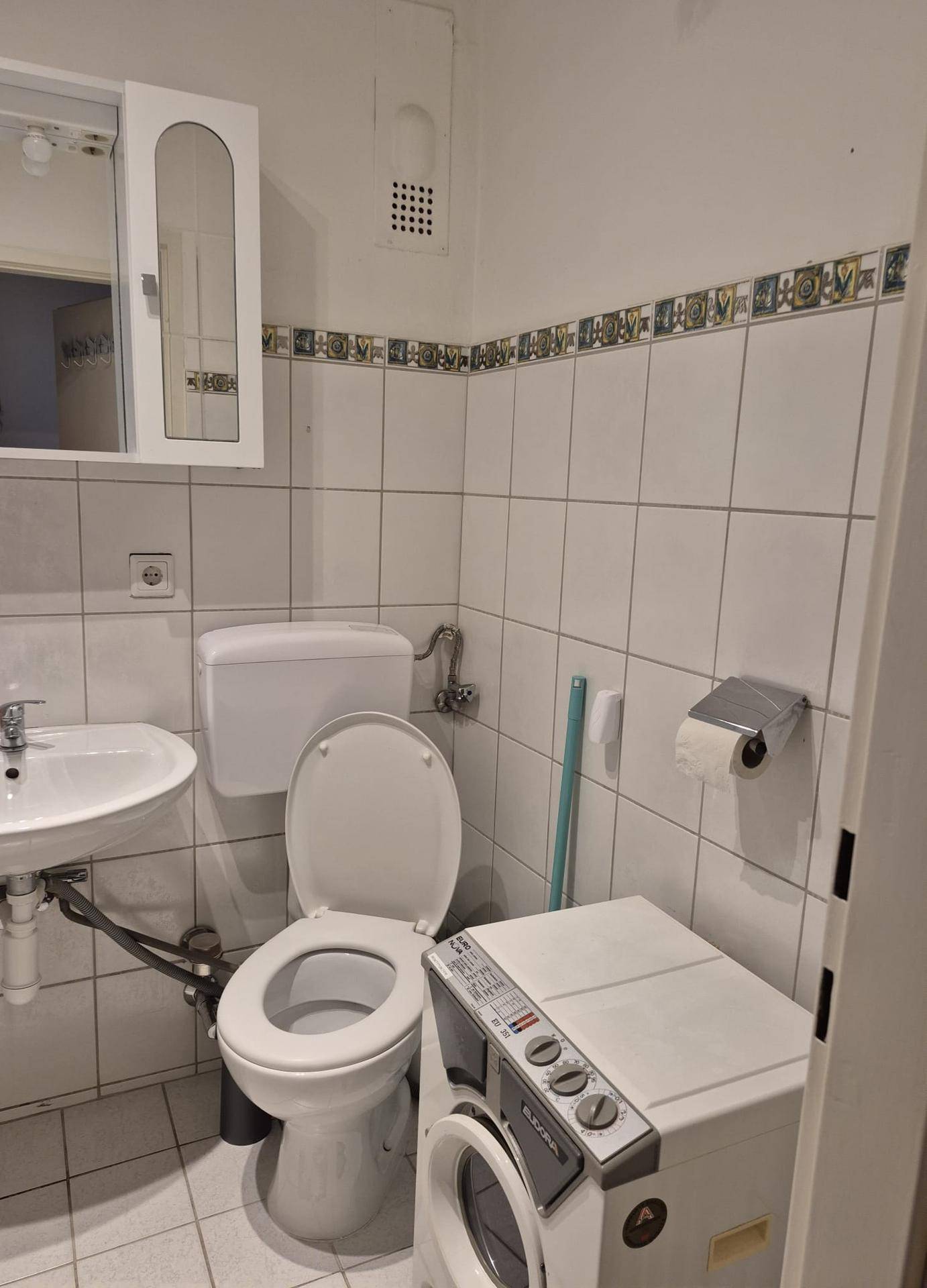 Badezimmer mit Toilette, Waschbecken und Waschmaschine, gefliesten Wänden.