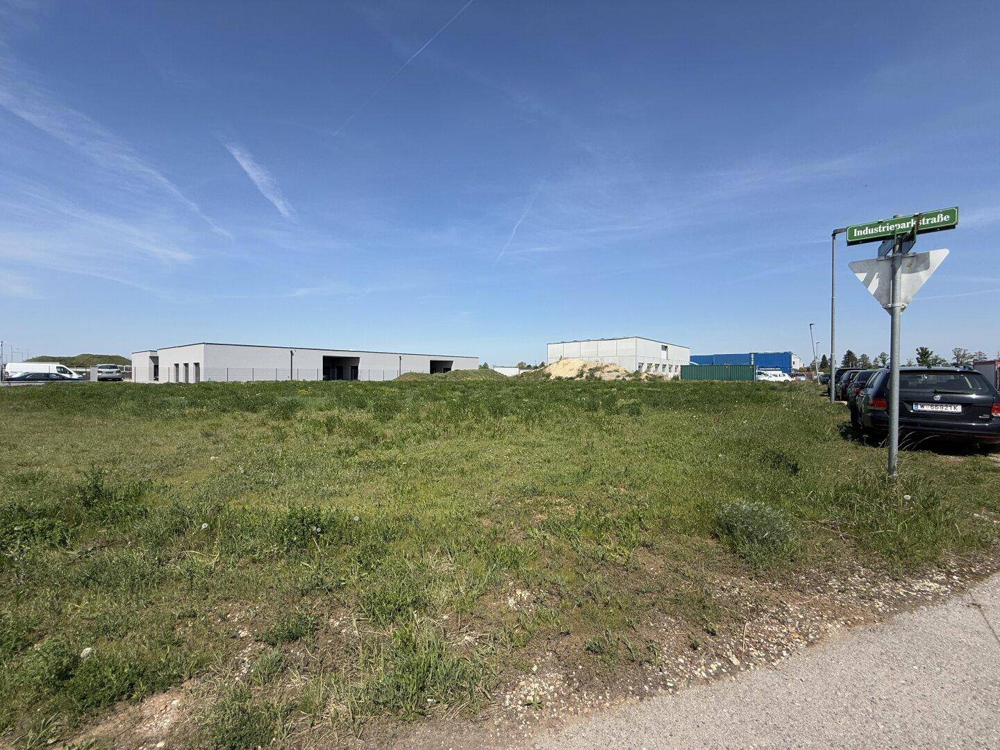 Großes, unbebautes Grundstück im Industriepark mit Grasfläche und einem Straßenschild im Vordergrund.