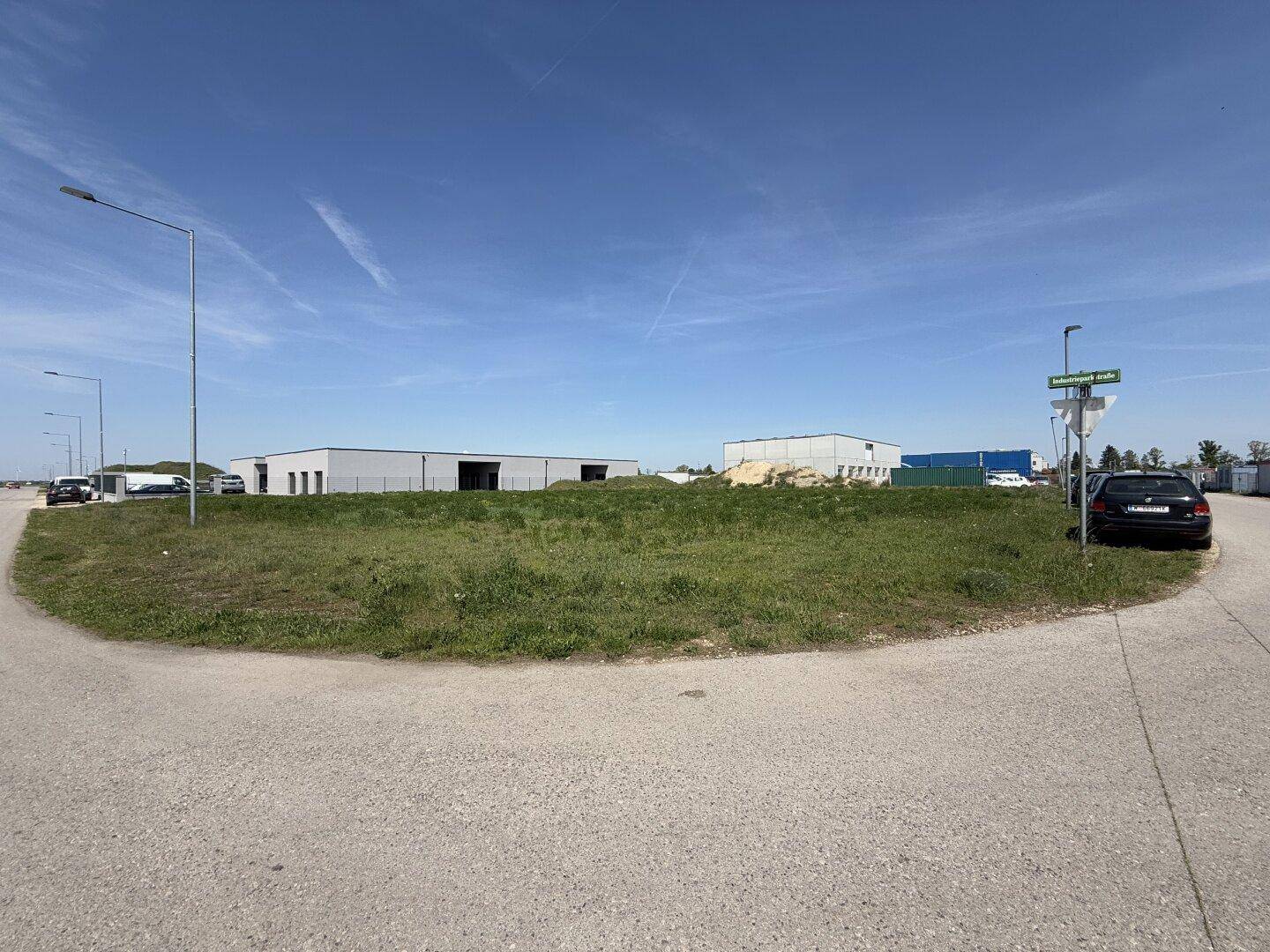 Weitläufiges, grünes Grundstück an einer Straße im Industriepark, umgeben von Gewerbegebäuden.