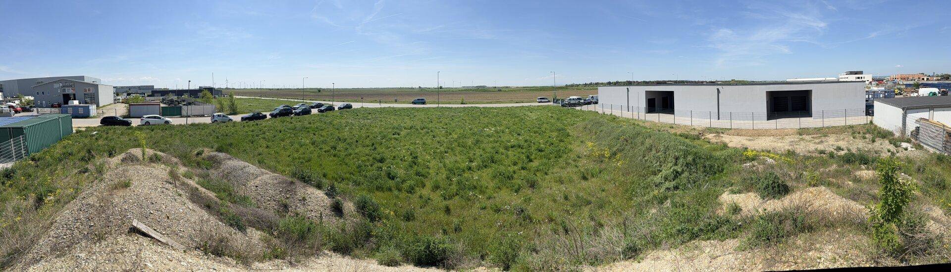 Panoramaansicht eines großen, grünen Grundstücks mit angrenzenden Gewerbegebäuden und Fahrzeugen.