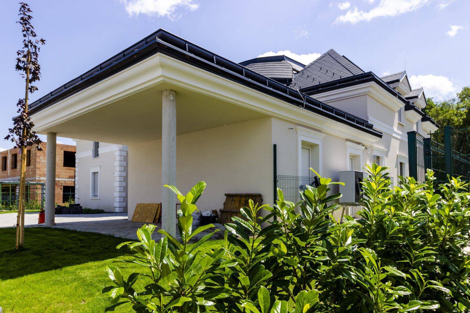 Seitenansicht der Villa mit überdachtem Carport und gepflegter Grünfläche.