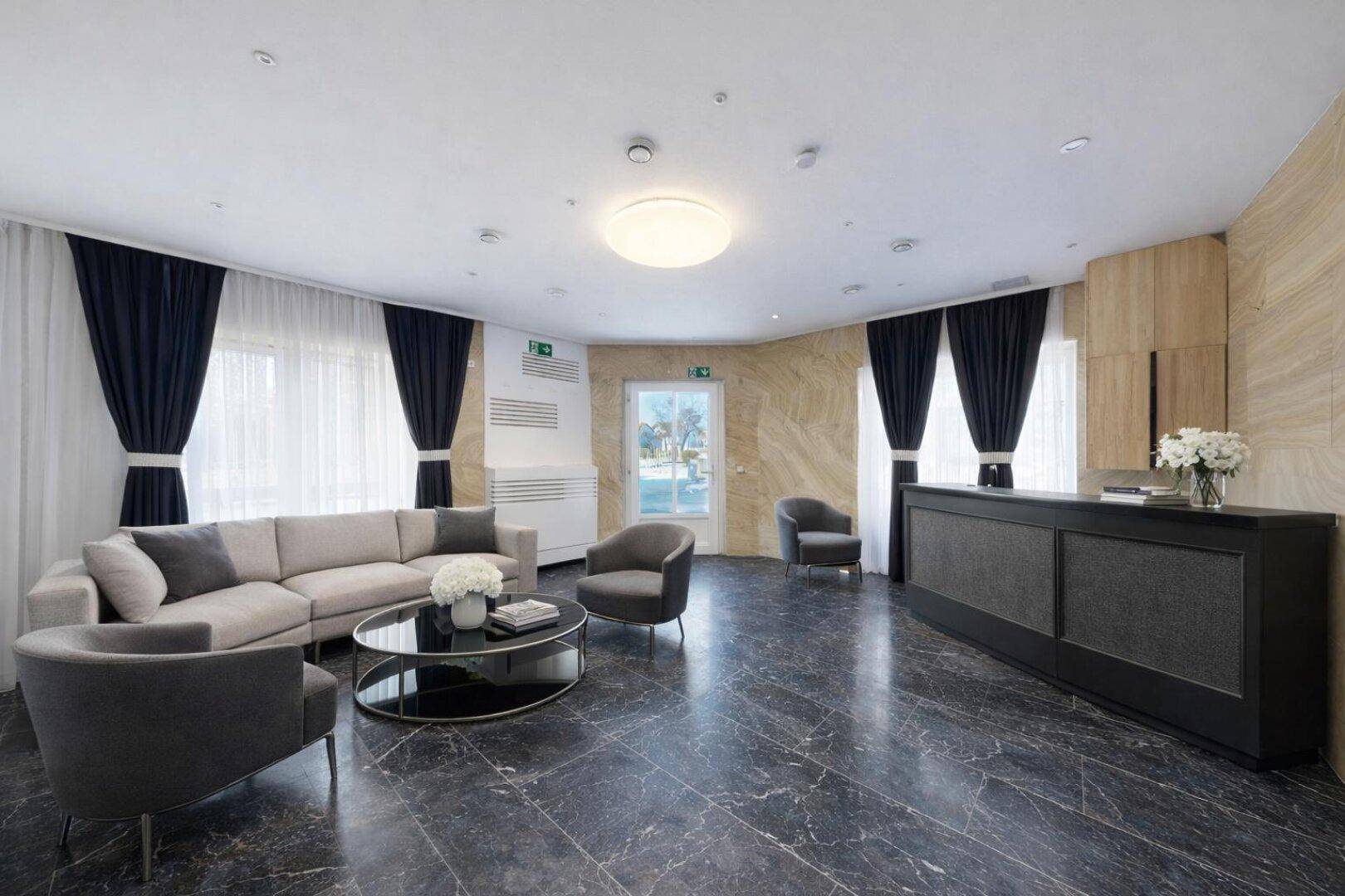 Geräumige Lobby mit dunklem Marmorboden, beigen Wänden und moderner Sitzgruppe.