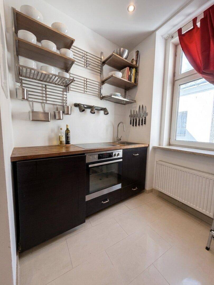Kleine Küche mit dunklen Unterschränken, Holz-Arbeitsplatte und offenem Regal.