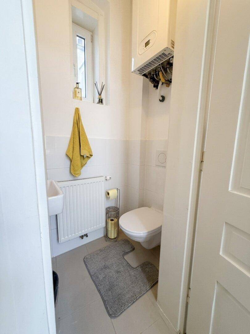 Kleines Gäste-WC mit Fenster, Toilette, Waschbecken und Heizkörper.
